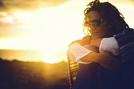 stockphotosideportraitofyoungprettywomanenjoyingsunsettimealonehuggingherkneesandlovingherself2149543569.jpg
