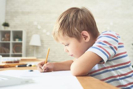 stockphotosideviewportraitofdiligentlittleboywritingordrawingcarefullysittingatdeskanddoing753961870.jpg