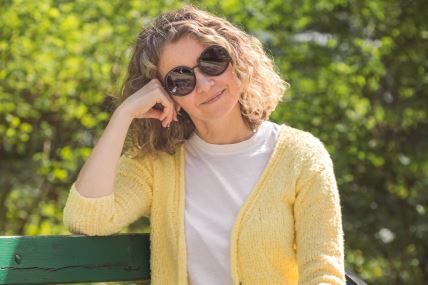 Žena sedi u parku na klupi u žutom džemperu i naočarama za sunce