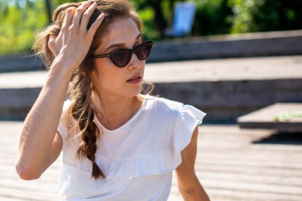 Devojka u beloj majici sa kikom i sa naočarama za sunce sedi u parku u gradu