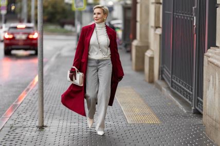 Žena srednjih godina šeta ulicom obučen au crveni kaput i sive pantalone