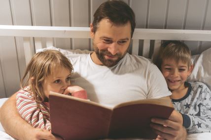 stock-photo-happy-mature-year-old-father-reading-book-to-his-curious-children-lying-in-a-bed-before-the-2703991929.jpg