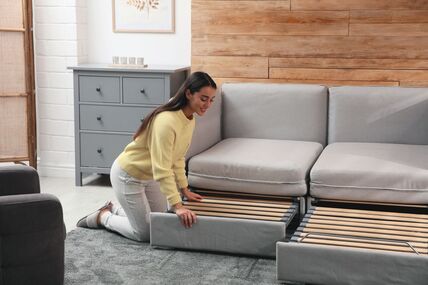 stock-photo-young-woman-unfolding-sofa-into-a-bed-in-room-modern-interior-2124270845.jpg