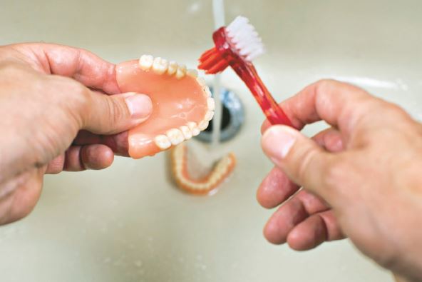 ciscenje-proteze-stockphotocleaningandwashingoftheteethdenturesinthesinkwiththerunningwaterandthetoothbrush1555441100.jpg