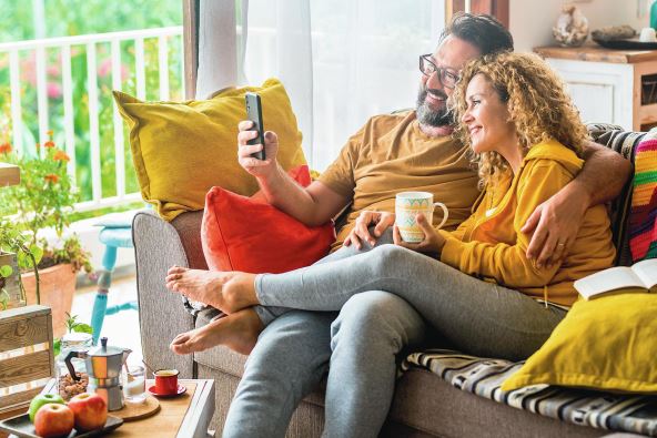 1--stockphotocaucasiancoupledoingvideocallwithmobilephoneathomesittingonthesofamanandwoman2171905675.jpg