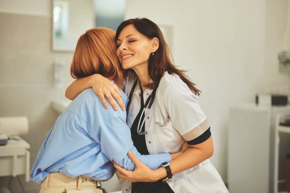 stockphotoafemaledoctorsmilingandhuggingafemalepatientsittingatthedoctorsoffice2381659987.jpg