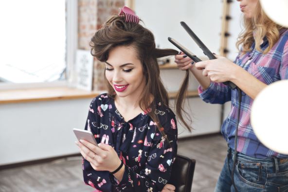 stalno-javljanje-na-mobilni-telefon--stockphotofemalehairdresserapplyinghairstraightenerforlonghairofsmilingyoungwomanusingsmartphone391326466.jpg