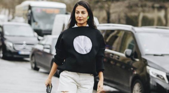 Moderna žena, crnka u gradu, šeta obučena u crnu duksericu i bele pantalone