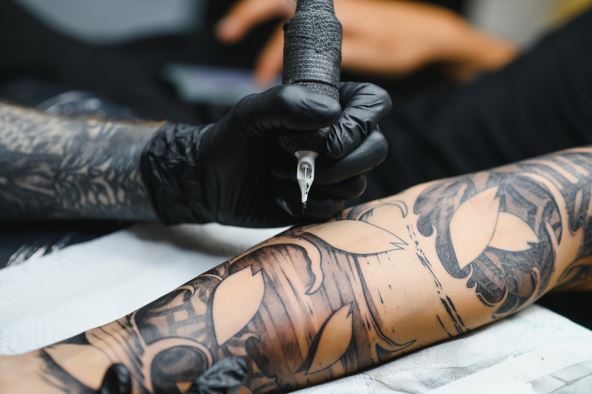 stock-photo-cropped-close-up-of-a-bearded-tattoo-artist-working-at-his-studio-tattooing-sleeve-on-the-arm-of-2125291070.jpg