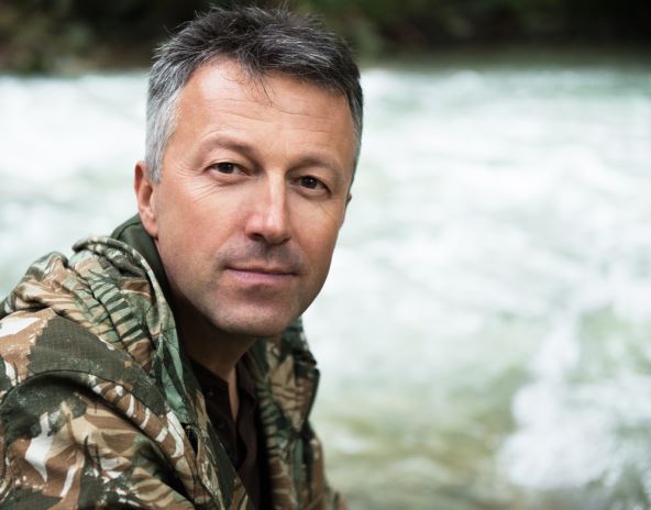 Muškarac u šarenoj košulji sedi napolju i gleda u kameru