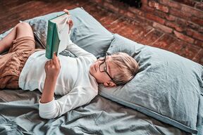 stock-photo-portrait-of-joyful-preschool-child-with-glasses-reading-a-book-and-lying-down-on-a-bed-in-living-1856696767.jpg